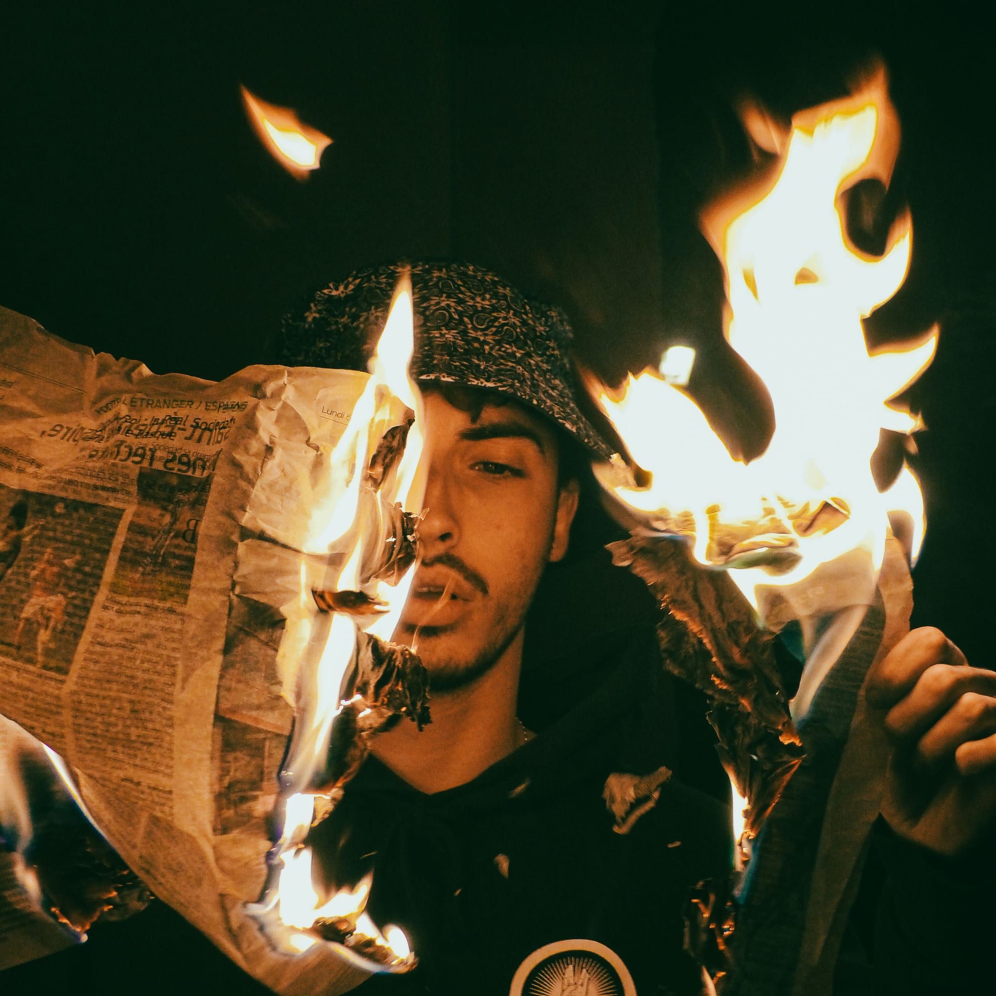 Ein junger Mann hält brennendes Zeitungspapier, Flammen umgeben sein Gesicht