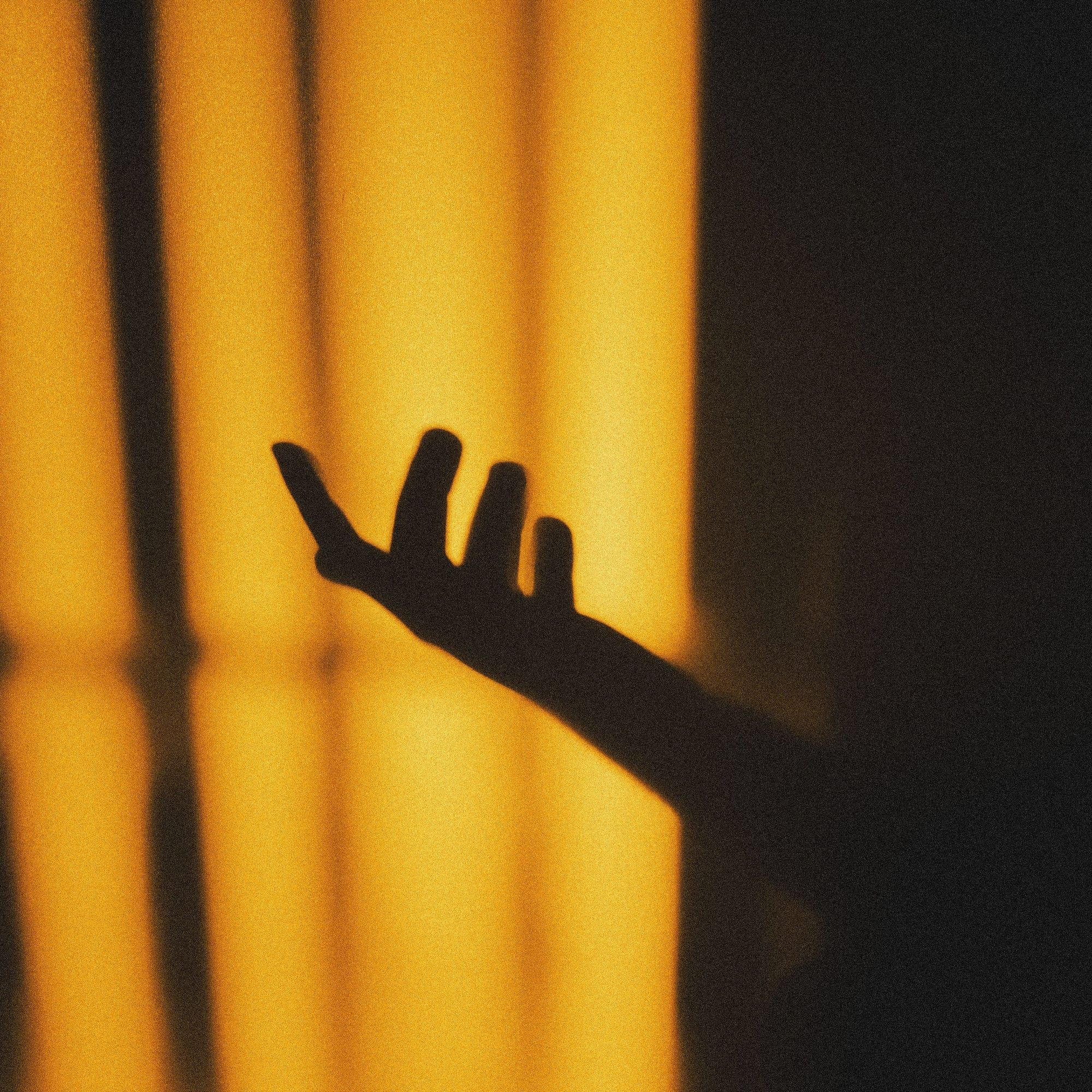 Der Schatten einer ausgestreckten Hand vor goldenem Licht, das wie durch Gitterstäbe fällt